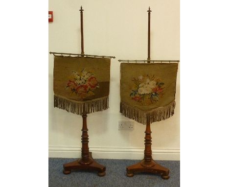 A pair of early Victorian mahogany Pole Screens, each with floral tapestry drape and on tripod base with squat bun feet 