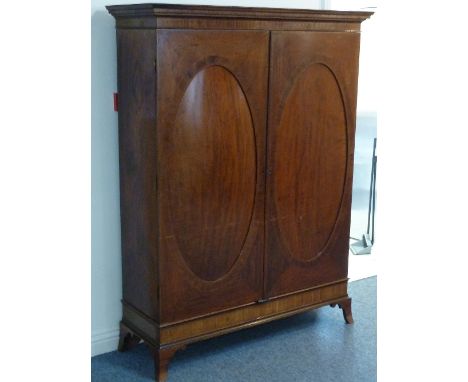A late 18th Century mahogany Wardrobe, the flaring cornice above two oval panelled crossbanded doors opening to reveal hangin