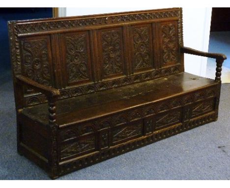 An antique oak Settle, the top rail centrally carved with a date 1677 above a five panelled front carved with flower heads an