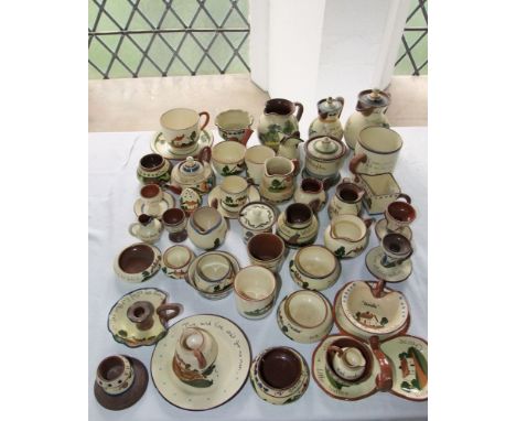 An extensive collection of Torquay pottery wares including a match holder/striker, chamber stick, two covered jugs, tea wares