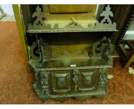 A mid-Victorian carved oak hanging wall shelf, the lower section enclosed by two panelled doors, with shaped and pierced deta