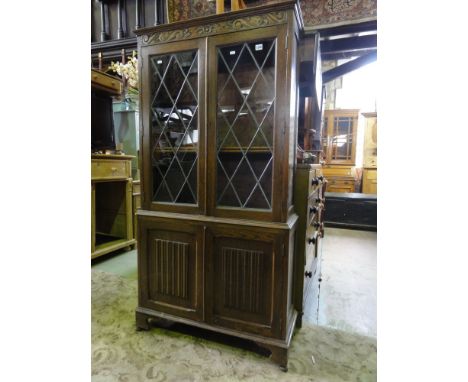 A reproduction oak side cupboard, freestanding and enclosed by two pairs of panelled doors, the lower with applied linen fold