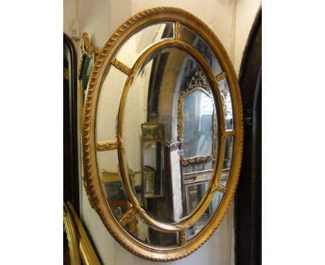 An Adam style wall mirror of oval form, the central mirror plate with bevelled edged borders surrounded by a further surround