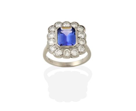 A Tanzanite and Diamond Cluster Ring, the emerald-cut tanzanite within a border of round brilliant cut diamonds, in white mil