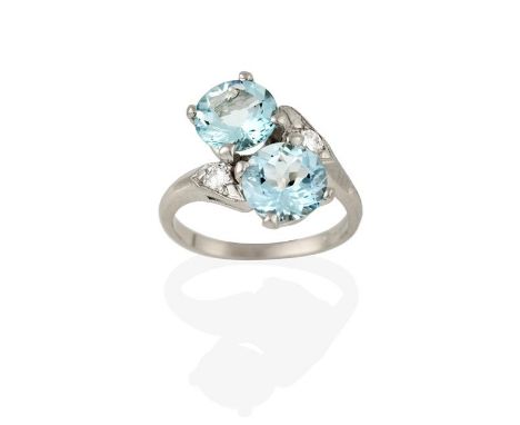 An Aquamarine and Diamond Ring, the round cut aquamarines diagonally set, in white claw settings, to a round brilliant cut di