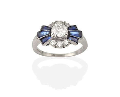 A Synthetic Sapphire and Diamond Cluster Ring, the round brilliant cut diamond flanked by tapered baguette cut synthetic sapp