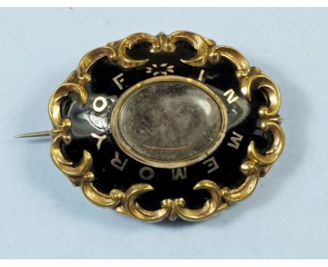A 19th century mourning brooch with gilt yellow metal scrolling border inset with black enamel and gilt script 'In Memory Of'