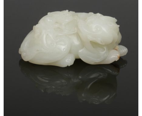 A Chinese Qing dynasty carved pale celadon jade model of a recumbent kylin. Modelled with its head turned backward looking to