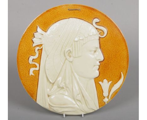 A Leeds Art Pottery circular cameo portrait plaque. Depicting the head of Cleopatra in profile against a mottled ochre ground
