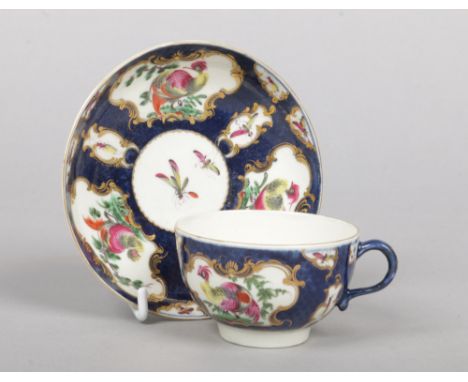 A Worcester teacup and saucer. Scale blue ground and with gilt cartouches containing painted birds and insects. Underglaze sq