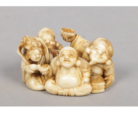 A Japanese Meiji period carved ivory netsuke. Formed as a seated group of figures eating. Signed, 6cm wide.