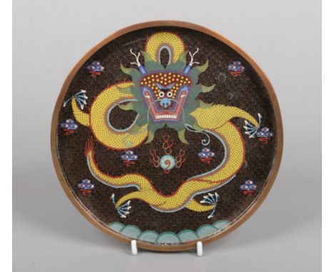 A Chinese copper and cloisonne enamel circular tray. Decorated on a black ground with a yellow dragon chasing a flaming pearl