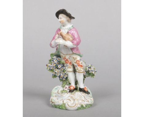 A Derby figure of a man playing bagpipes. Decorated in coloured enamels, stood before a floral bocage on a Rococo style base 
