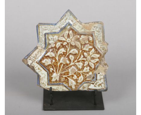 An antique Kashan star shaped tile on stand. Moulded with flowers and glazed in tones of turquoise and brown and with a borde
