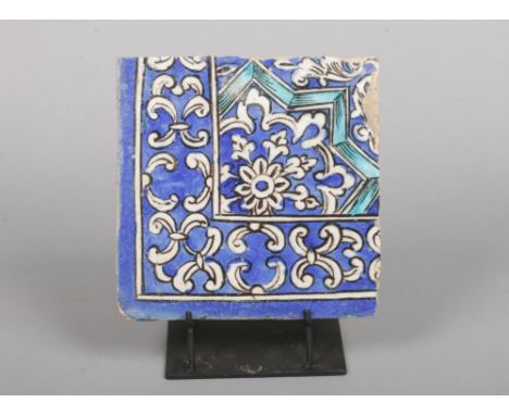 An antique Turkish Iznik style corner tile on stand. Glazed in tones of blue and turquoise, 21.75cm square.
