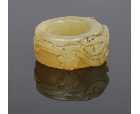 A Chinese jade coloured hardstone archers ring. Carved around its circumference with a mythical beast, 3.75cm wide.