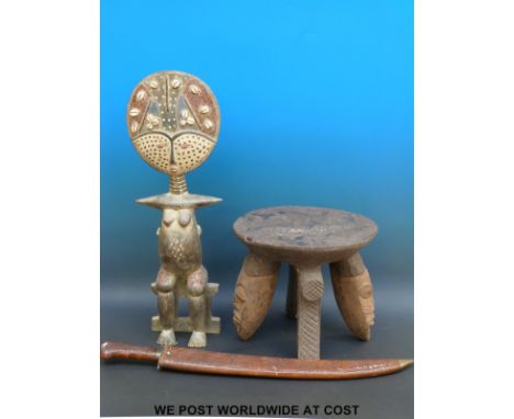 A carved African stool with masked legs together with a fertility figure inset with cowrie shells and a curved sword in a car