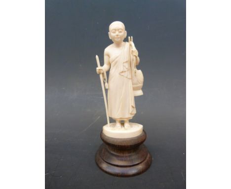 An early 20thC carved Indian ivory figure of a Buddhist monk holding a stick, prayer beads and a drum, set on a rosewood base