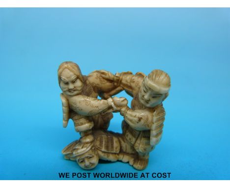 A Japanese Meiji period carved ivory netsuke of two Samurai fighting on the back of another Samurai who when viewed from bene