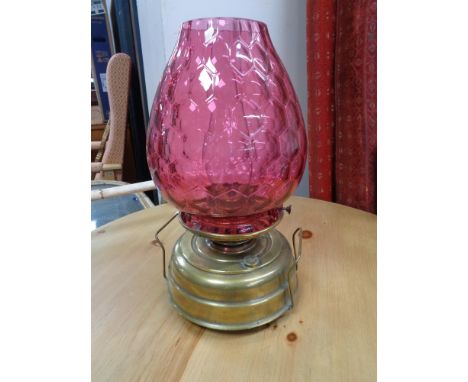 An antique brass paraffin lamp with cranberry glass shade