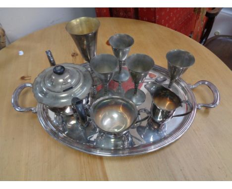 A chrome twin handled serving tray containing plated wares, three piece plated tea service etc 
