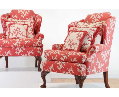 A pair of George II-style wingback armchairs, 20th century, each upholstered in coral-decorated fabric, raised on knee-carved