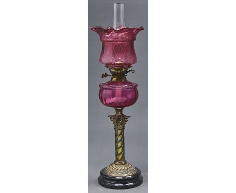 A Victorian oxidised brass columnar oil lamp, on black glazed earthenware foot, with cranberry glass sack shaped fount and br
