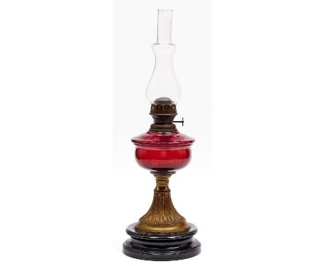 An Edwardian brass oil lamp, embossed with leaves, cranberry glass fount, on black glazed earthenware foot, brass burner, 31c