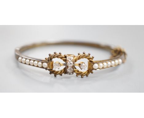 A late Victorian yellow metal, six stone diamond cluster set hinged bangle, with split pearl set shoulders, interior diameter