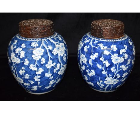 A LARGE PAIR OF CHINESE GINGER JARS with carved hardwood lids, underglaze blue painted decoration of prunus blossom on a crac