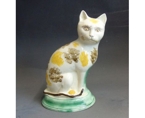 A Staffordshire pottery model of a cat with yellow and brown sponged decoration sitting on a green basecirca 1785, 22cm highC