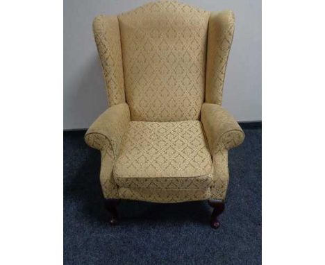 A wing backed armchair by Jade upholstered in golden fabric 