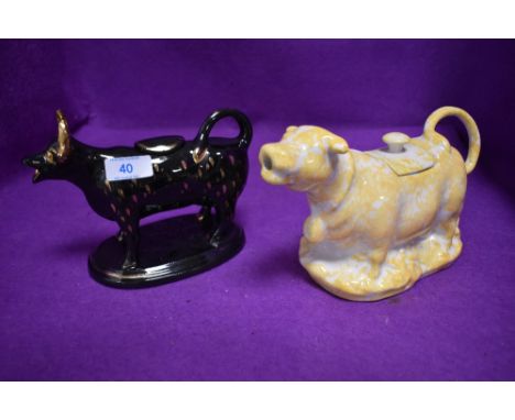 Two ceramic creamers in the form of cows one black and one yellow glazed