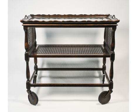 An oak two tiered dinner trolley with a glass top and cane work tier and drop sides together with a similar oak book trough (