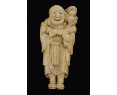 Japanese carved ivory netsuke, signed Yoshitomo and depicting a monkey trainer, a drum before him and a monkey on his shoulde