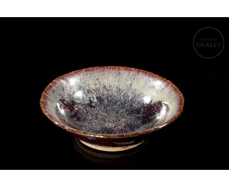 A ceramic bowl with a circular base and a deep body, widening at the mouth and ending in a jagged rim. It is covered with a t
