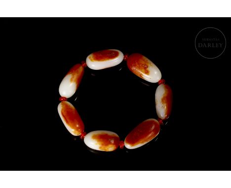 White jade beads with reddish spots and carved amber. They have an elongated shape with rounded edges, pierced by a thin cent