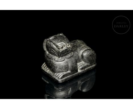 Stone carving in the form of an archaic lion, with its body drawn up on its bent legs, and its large head cocked to one side.