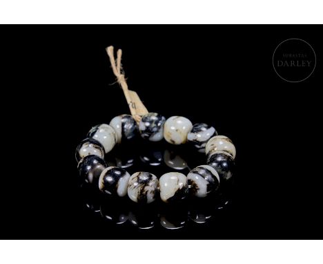 Thirteen round-shaped carved jade beads, characterised by their white colour with dark and ochre veins. Linked by a cord. Wei