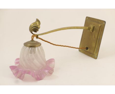 Manner of WAS Benson, an Arts and Crafts period brass wall lamp, sinuous arm with scallop shell terminal supporting a pink fr