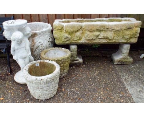 A reconstituted stone trough shaped planter, a circular planter, a large circular planter and a planter on a trio of children