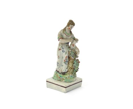 A Staffordshire figure of a shepherdess, c.1800, standing and tending a lamb which sits atop a tree trunk beside her, raised 