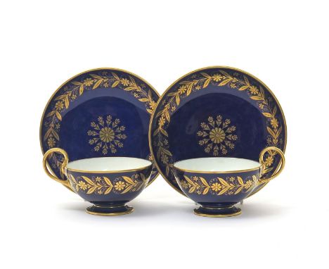 A pair of Sèvres cups and saucers, 2nd half 19th century, decorated with a continuous formal gilt band of leaves and flowers 