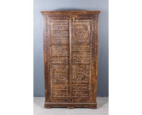 An Indian Panelled Hardwood Cupboard, with moulded cornice, fitted three shelves enclosed by a pair of doors carved with figu