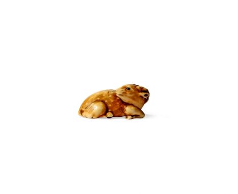† A JAPANESE IVORY NETSUKE, 19TH CENTURY Carved as a recumbent sika deer, its head turned to dexter, the eyes inlaid, signed 