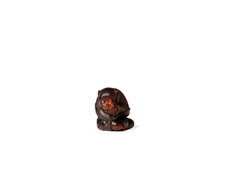 † A JAPANESE WOOD NETSUKE, 19TH CENTURY Carved as a monkey biting a large biwa fruit and holding another one between his feet