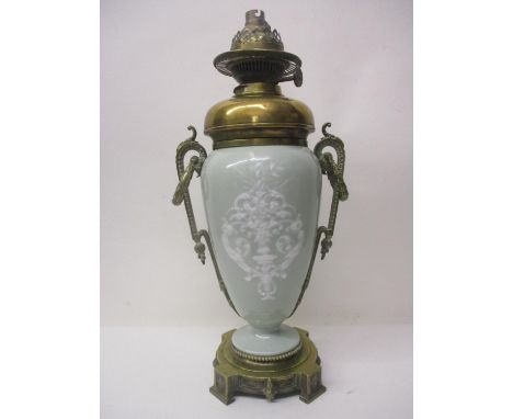 A late 19th century French pate sur pate and brass oil lamp of ovoid form, with twin loop and wreath handles, on a base, conv
