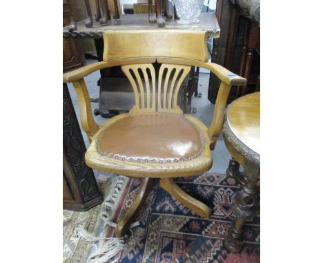 An early 20th century light oak rotating desk chair, raised on splayed legs and castors 