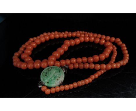 A graduated coral bead necklace with a carved jade clasp, stamped silver, 68cm long 