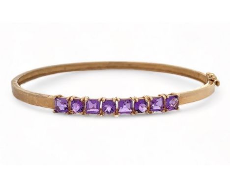 A small 9ct gold hinged bangle set with eight purple gemstones, likely CZs, alternating square cut and checkerboard cut. Birm